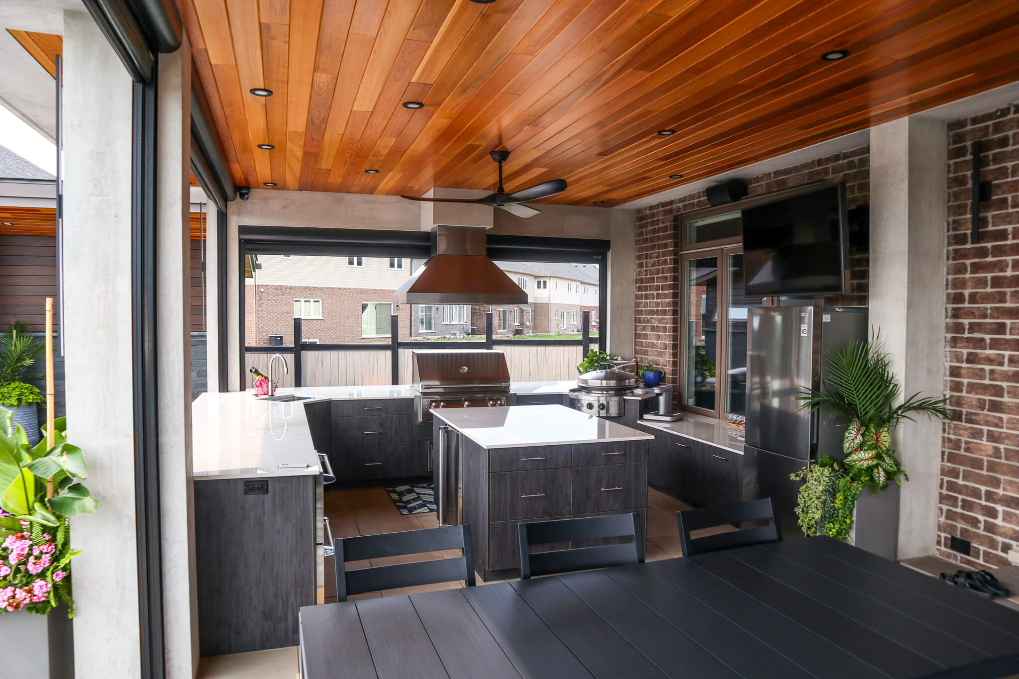 Luxury covered outdoor kitchen featuring wood ceiling, stainless grill, modern cabinetry, and bar seating beside a dining area.