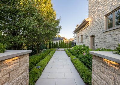 A formal stone walkway framed by layered planting and subtle lighting, designed to create structure, flow, and quiet elegance.