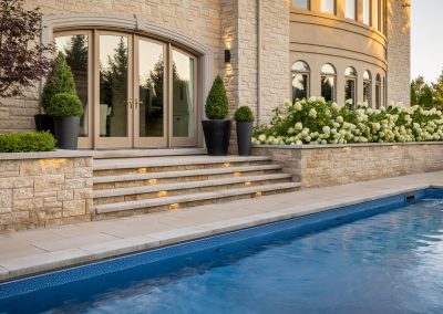 A refined poolside terrace featuring layered stonework, integrated lighting, and structured planting that connects architecture and outdoor living.
