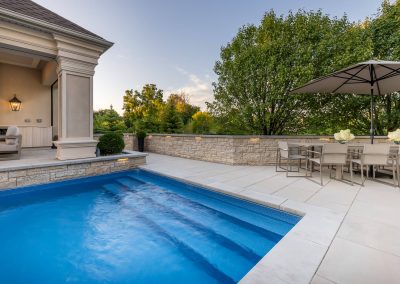 A clean-lined poolside dining terrace designed for entertaining, featuring stone walls, expansive paving, and seamless indoor-outdoor flow.