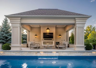 An open-air poolside cabana designed for entertaining, featuring integrated lighting, lounge seating, and a seamless connection to the surrounding patio and pool.