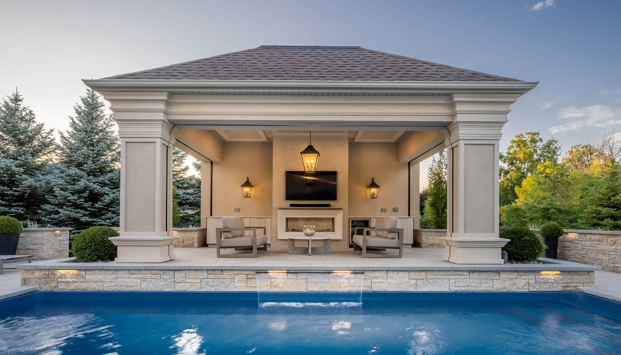 An open-air poolside cabana designed for entertaining, featuring integrated lighting, lounge seating, and a seamless connection to the surrounding patio and pool.