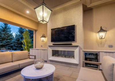 An open-air cabana lounge featuring a built-in fireplace, integrated media, and refined finishes, creating a comfortable poolside retreat designed for extended seasonal use.