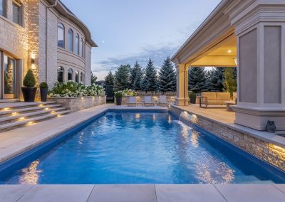 An open-air cabana anchors this poolside design, combining architectural lighting, clean stonework, and seamless transitions between the home and outdoor living spaces.