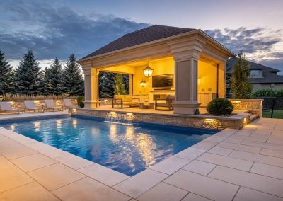 A refined open-air cabana frames this illuminated poolscape, blending clean stonework, subtle water features, and purposeful lighting into a cohesive outdoor living space.