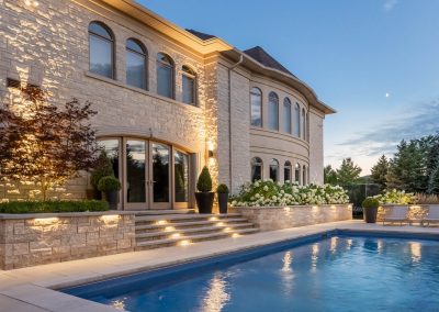 A refined poolside terrace showcases curved stone architecture, integrated step lighting, and layered planting design, creating a seamless transition between the home and outdoor living space.