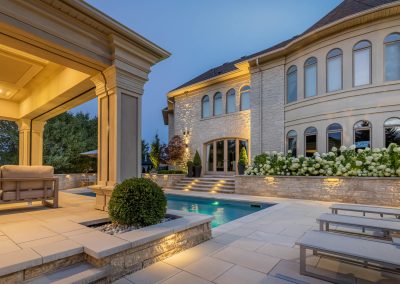 An integrated pool terrace combines stone hardscaping, layered lighting, and a covered pavilion to create a refined and cohesive outdoor living space.