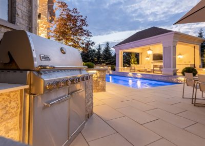 An outdoor kitchen paired with a poolside pavilion creates a functional gathering space that balances cooking, entertaining, and relaxed evening use.
