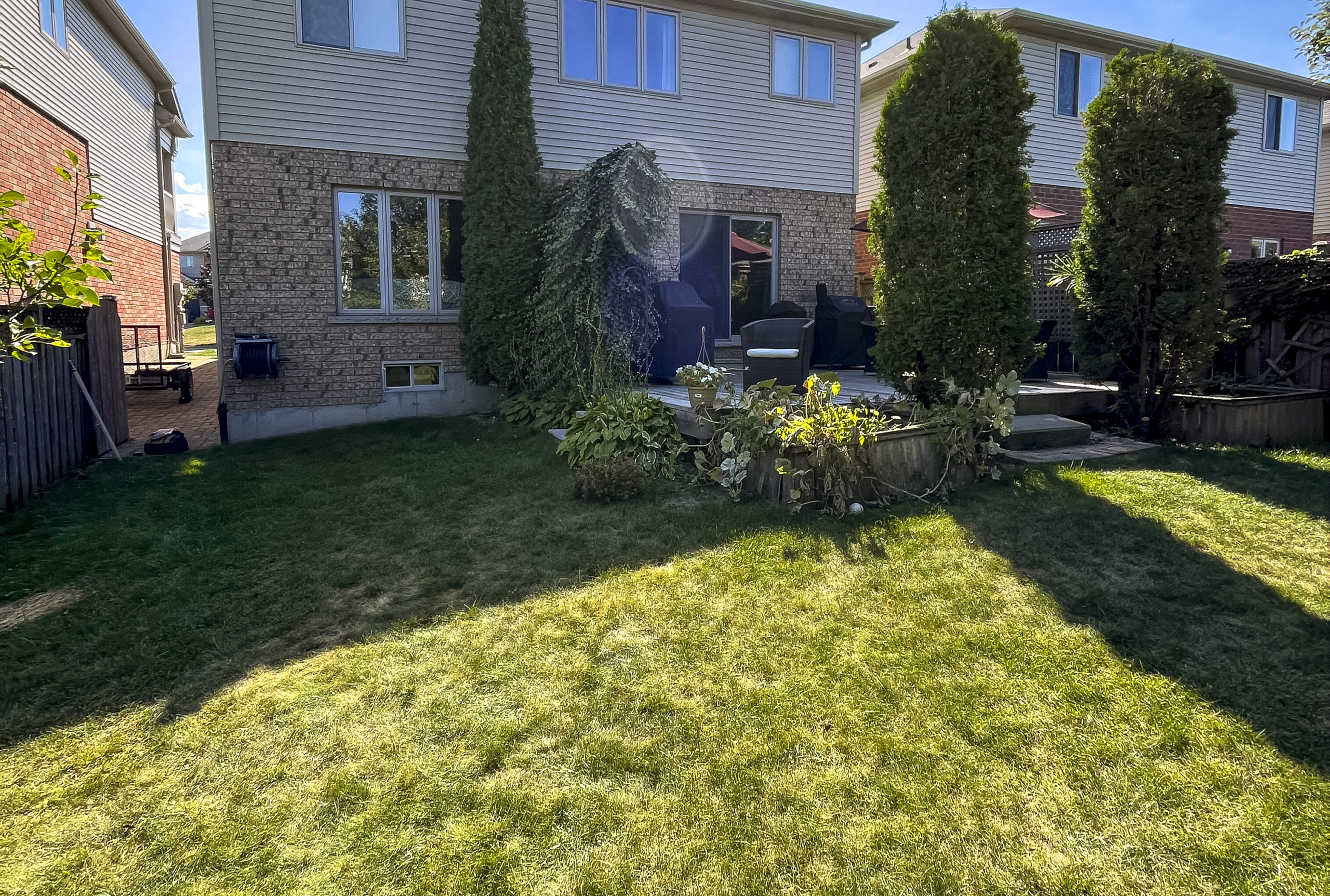 Backyard Before Landscape Renovation and Patio Build Original backyard before renovation, showing a sloped lawn, small patio, and existing plantings behind a suburban home