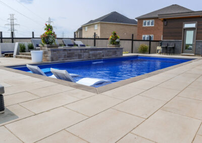 Backyard pool surrounded by beige Para HD slabs, raised stone water feature, in-pool loungers, and modern fencing.