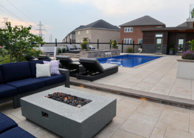 Outdoor seating area with navy sectional and concrete fire table overlooking the swimming pool and landscaped yard.