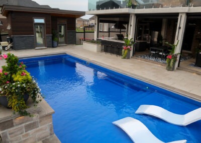Expansive patio surrounding a blue pool with Beige Para HD slabs, outdoor kitchen structure, planters, and lounge seating.