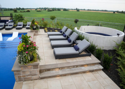 Raised terrace featuring grey loungers, Banas coping steps, planters, and views of landscaped greenery.