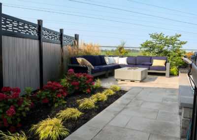 Backyard lounge area featuring navy outdoor sectional seating, a concrete fire table, ornamental grasses, and privacy fencing with decorative panels.