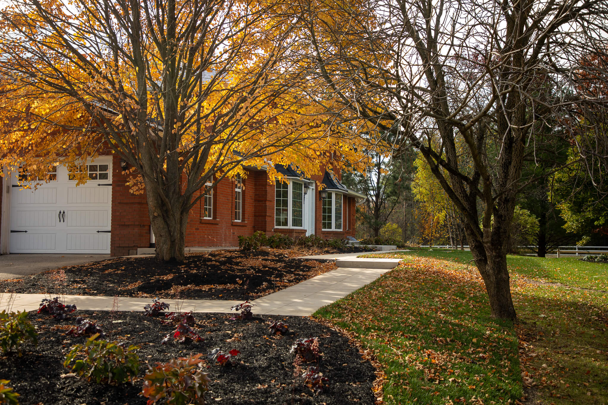 New front walkway and garden beds at the Mountsberg residence, featuring Permacon stone, refreshed plantings, and mature trees integrated into the landscape design