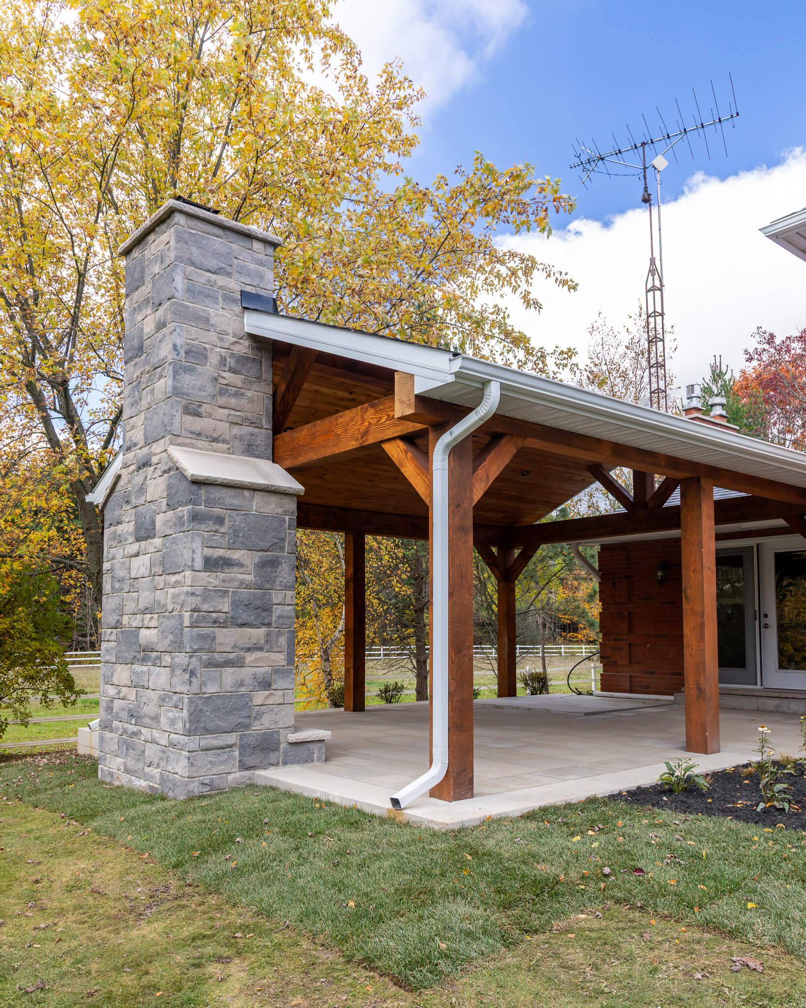 Covered backyard patio featuring a custom wood-burning fireplace, Douglas fir timber structure, and stone flooring at Project Mountsberg.