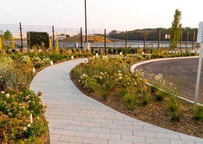 Curved stone walkway with native planting beds at the Porsche Experience Centre Toronto, designed to complement the architecture and vehicle-focused environment.
