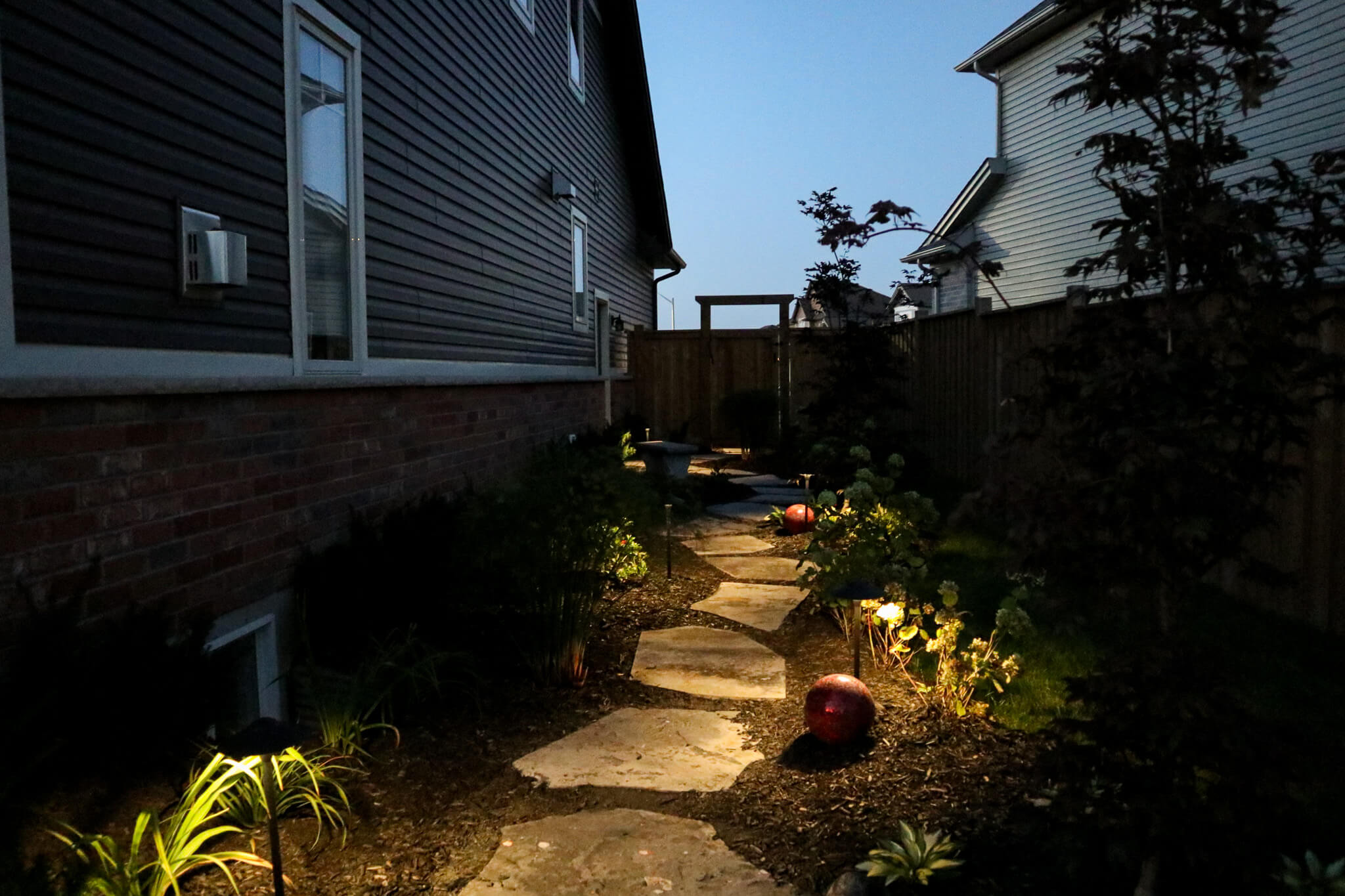 Soft landscape lighting illuminating a natural stone garden path with low-profile fixtures highlighting plants and guiding the walkway at dusk