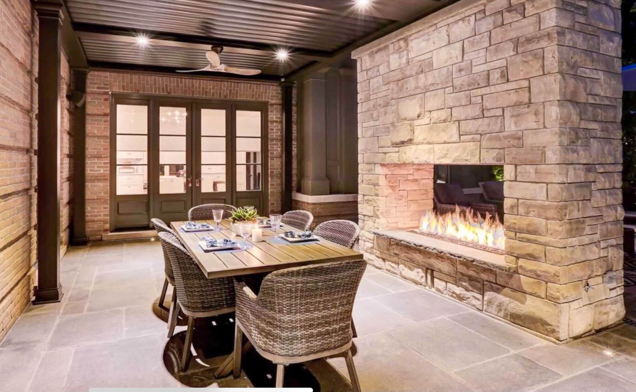 Covered outdoor patio featuring a built-in gas fireplace, stone masonry surround, and dining area beneath a roof with recessed lighting and ceiling fan.